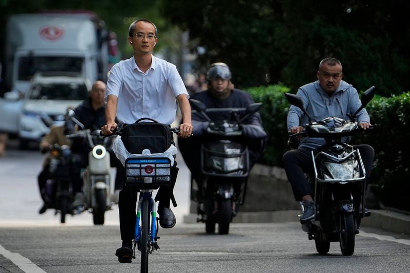 A man rides along motorists as they head to work during the morning rush hour in Beijing, Friday, Sept. 13, 2024. (AP Photo/Andy Wong)