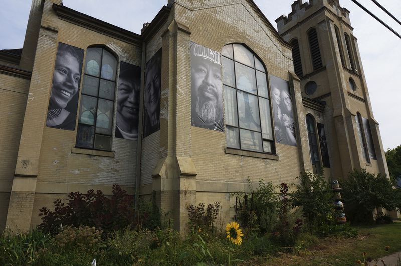 Large banners featuring congregants, including Lizete Vega, church council president, left, as part of a project on "belonging," adorn one side of Iglesia Luterana San Pablo in Minneapolis, on Sept. 8, 2024. (AP Photo/Giovanna Dell'Orto)