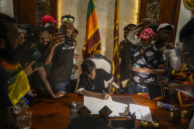 A protester sits at the desk of Sri Lankan Prime Minister Ranil Wickremesinghe after storming his office in Colombo, Sri Lanka, Wednesday, July 13, 2022. (AP Photo/Rafiq Maqbool, File)