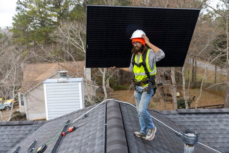 Joe McClain, an installer for Creative Solar USA, moves solar panels onto the roof of a home in Ball Ground, Georgia on December 17th, 2021.