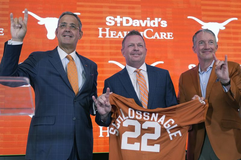Jim Schlossnagle, center, stands with Texas Athletic Director Chris Del Conte, left, and Texas president Jay Hartzell, right, after he was introduced as the new NCAA college head baseball coach at Texas, Wednesday, June 26, 2024, in Austin, Texas. Schlossnagle left rival program Texas A&M. (AP Photo/Eric Gay)