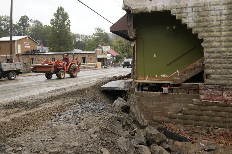 A person driving a front in loader passes a heavily one of several heavily damaged buildings along Bridge Street as clean up begins in the aftermath of Hurricane Helene Tuesday, Oct. 1, 2024, in Hot Springs, N.C. (AP Photo/Jeff Roberson)