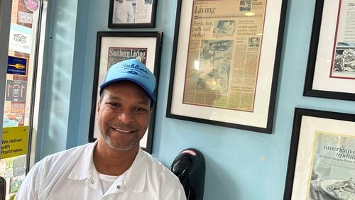 Kamal Grant, owner of Sublime Doughnuts in North Druid Hills and West Midtown, poses on June 4, 2024 with a 2009 review of his location by former AJC food critic John Kessler he said helped boost his business. RODNEY HO/rho@ajc.com