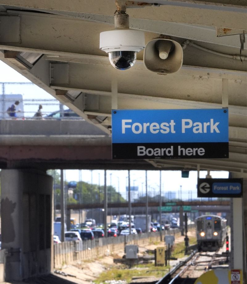 A security camera and speaker hang from the ceiling of the Chicago Transit Authority Harlem Ave. station as a Blue Line train approaches the station heading West to the Forest Park, Ill., station, as two pedestrians walk toward the station, Tuesday, Sept. 3, 2024, in Forest Park, Ill. (AP Photo/Charles Rex Arbogast)