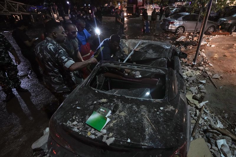 Policemen and civil defense workers inspect a damaged car near a building that was hit in an Israeli airstrike, in Beirut, Lebanon, early Monday, Sept. 30, 2024. (AP Photo/Bilal Hussein)