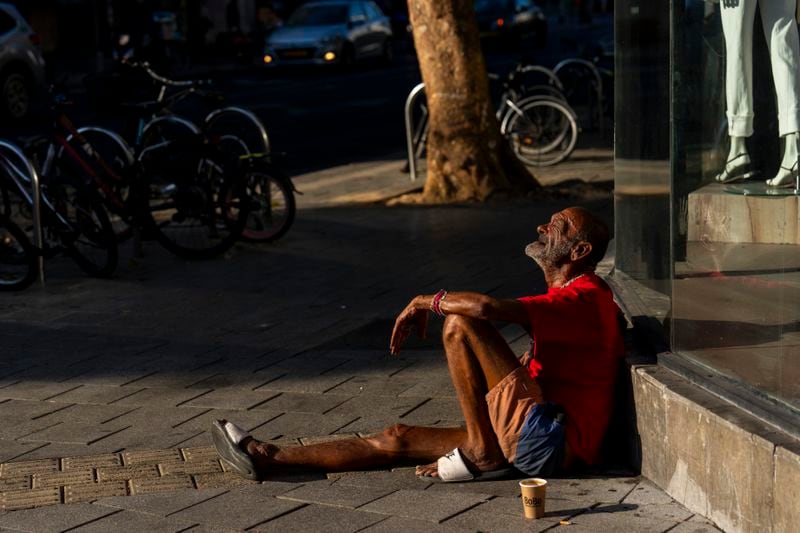 A person sits on the sidewalk next to a mall in Tel Aviv, Israel, Thursday, Aug. 15, 2024. Israel's economy is suffering from the nearly 11-month war with Hamas, as its leaders grind ahead with its offensive in Gaza that threatens to escalate into a wider conflict. (AP Photo/Ariel Schalit)