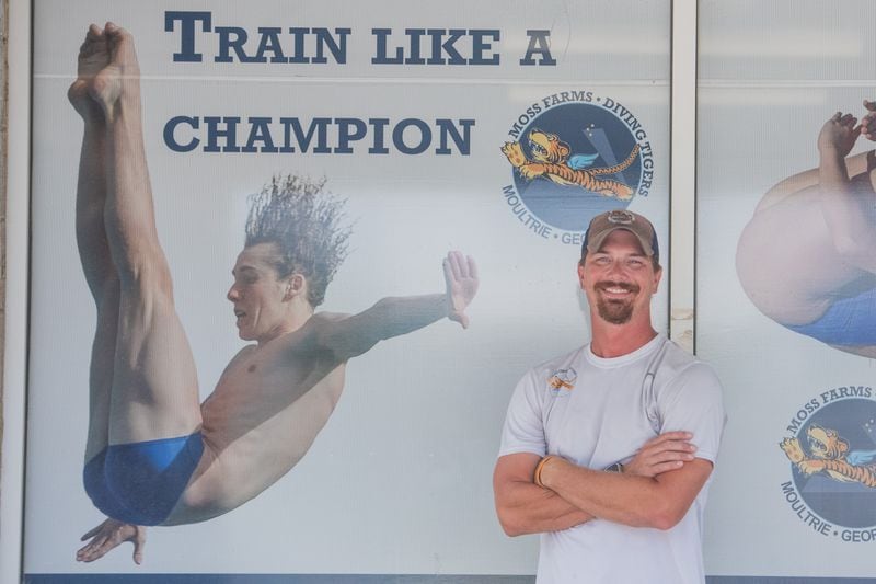 Tom Gimm, head diving coach at Moss Farms Diving pose for a picture next to a poster of Carson Tyler in Moultrie on Wednesday, July 24, 2024.  (Ziyu Julian Zhu / AJC)