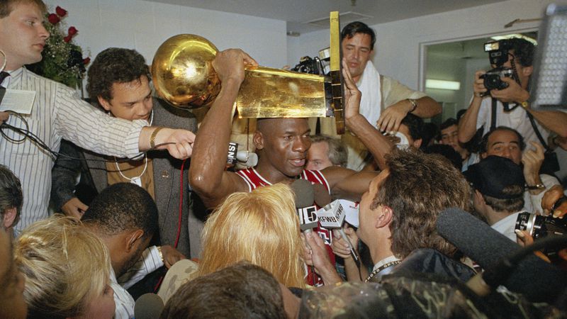 Chicago Bulls Michael Jordan holds the NBA Championship trophy aloft while talking with the media in the locker room after clinching the title with an 108-101 win against the Los Angeles Lakers Wednesday, June 13, 1991, at Inglewood, Calif. (Reed Saxon/AP)