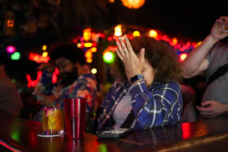 A patron puts their hand to their face as Republican presidential candidate former President Donald Trump speaks about how he would handle the Israel-Hamas war as people watch the presidential debate at Hula Hula, a tiki themed karaoke bar, Thursday, June 27, 2024, in Seattle. (AP Photo/Lindsey Wasson)