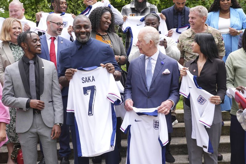 King Charles III (centre) with Idris Elba (centre left) and young people hold England football team shirts in support of the England football team as they attend an event for The King's Trust to discuss youth opportunity, at St James's Palace in central London, Friday July 12, 2024. The King and Mr Elba, an alumnus of The King's Trust (formerly known as The Prince's Trust), are meeting about the charity's ongoing work to support young people, and creating positive opportunities and initiatives which might help address youth violence in the UK, as well as the collaboration in Sierra Leone between the Prince's Trust International and the Elba Hope Foundation. (Yui Mok/pool photo via AP)