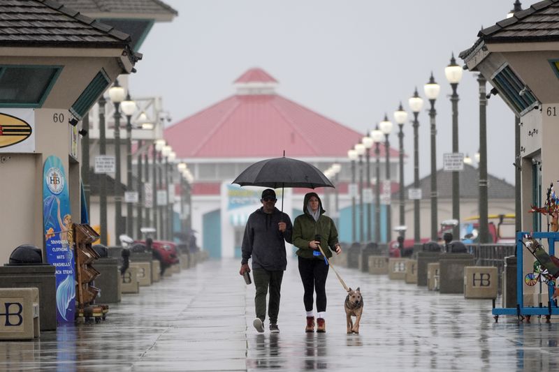 FILE - A couple walk in the rain with their dog along the Huntington Beach Pier in Huntington Beach, Calif., on Feb. 6, 2024. (AP Photo/Marcio Jose Sanchez, File)