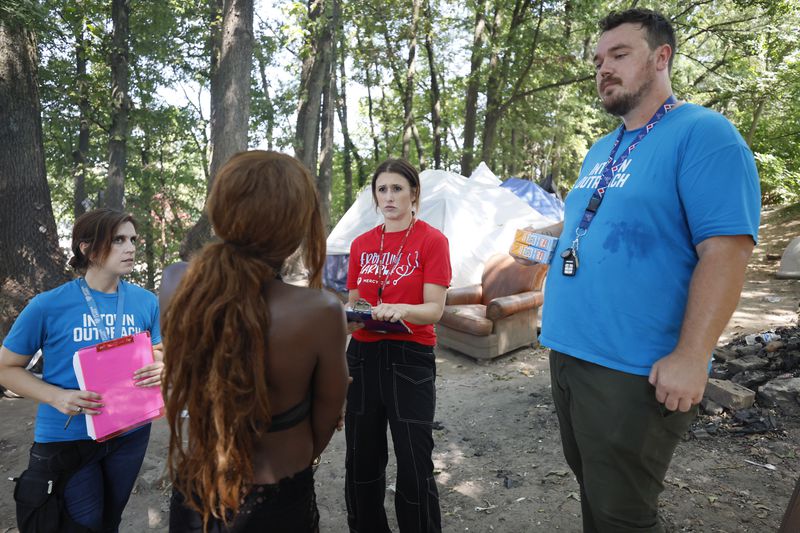 From left to right, Tracy Woodard from Intown Cares; Lauren Hopper, a street medicine nurse from Mercy Care; and Cody Wallace from Intown Cares provide outreach at the Cooper Street encampment on Monday, Aug. 12, 2014. They were helping someone schedule an appointment to visit a clinic. (Miguel Martinez / AJC)