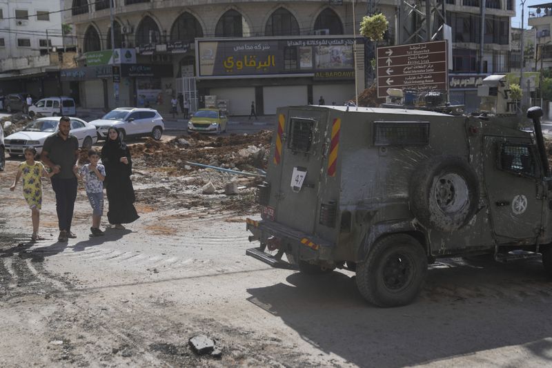 Palestinians walk past an Israeli armored vehicle during a military operation in the West Bank city of Tulkarem, Wednesday, Sept. 4, 2024. (AP Photo/ Nasser Nasser)