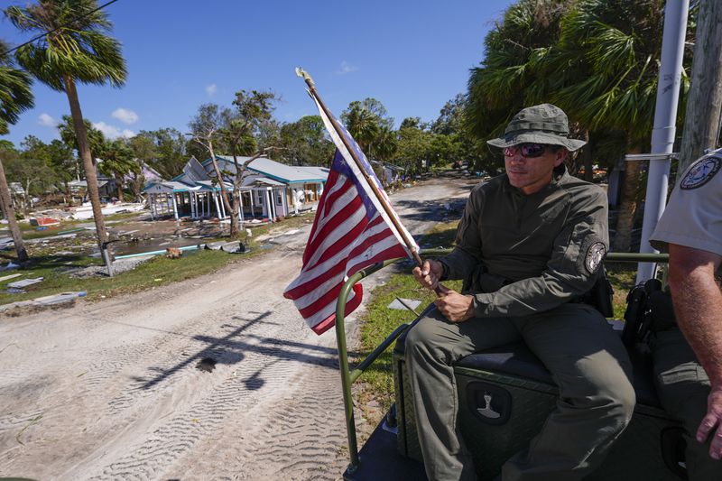 Officer Nate Martir, a law enforcement officer from the Florida Fish Wildlife and Conservation Commission, holds an American flag that was lying on the ground amid debris, while patrolling from a high water capable swamp buggy, in the aftermath of Hurricane Helene, in Cedar Key, Fla., Friday, Sept. 27, 2024. (AP Photo/Gerald Herbert)