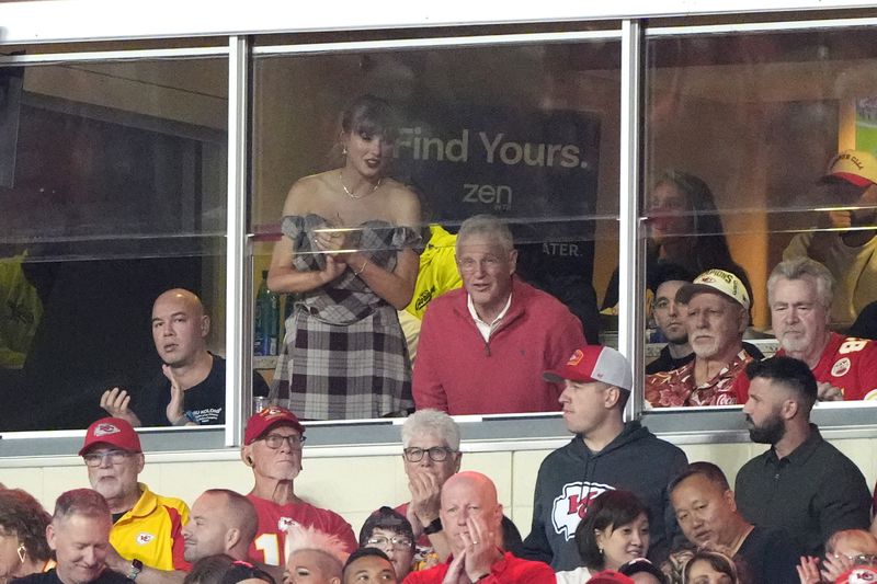 Taylor Swift stands as she watches from a suite next to her dad Scott Swift during the first half of an NFL football game between the Kansas City Chiefs and the New Orleans Saints Monday, Oct. 7, 2024, in Kansas City, Mo. (AP Photo/Charlie Riedel)