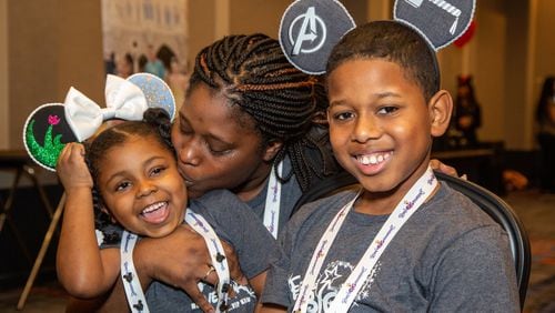 Kiki Troutman, 5, gets a kiss from her mother, Teneaski, while her brother Keon smiles as families gather at the Hilton Atlanta Airport the night before heading to Disney World for 2020 Bert’s Big Adventure. Photo by Phil Skinner