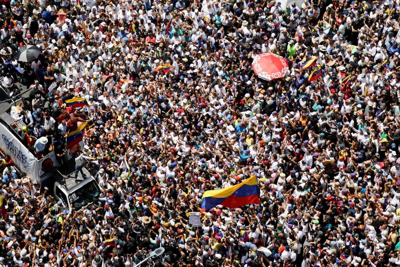 Opposition leader Maria Corina Machado, lower right, waves a Venezuelan national flag, during a rally to protest official results that declared President Nicolas Maduro the winner of the July presidential election, in Caracas, Venezuela, Saturday, Aug. 17, 2024. (AP Photo/Cristian Hernandez)