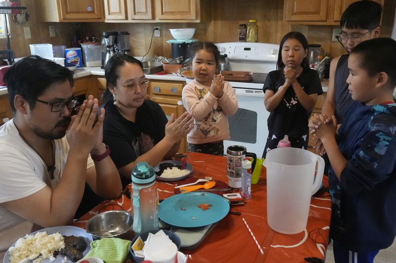 Bosco and Jennifer Carl say grace with their children before a meal at their home on Saturday, Aug. 17, 2024, in Mertarvik, Alaska. (AP Photo/Rick Bowmer)