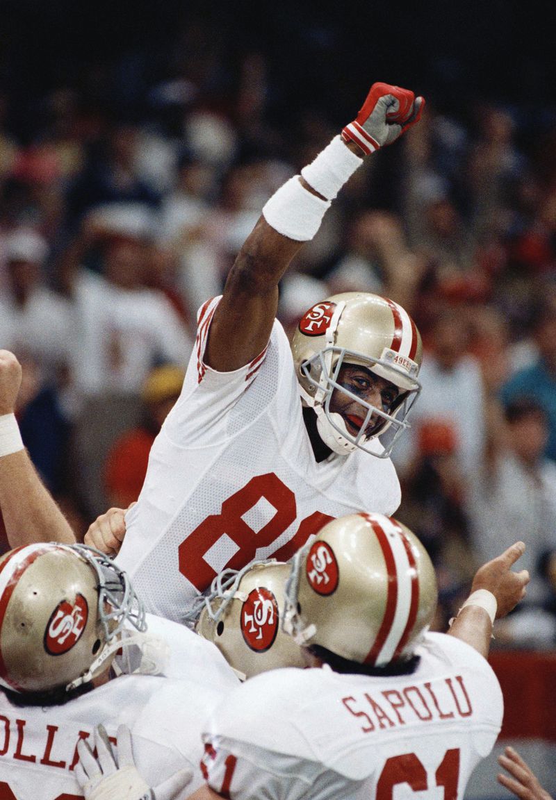 FILE - San Francisco 49ers wide receiver Jerry Rice raises his fist after scoring his second touchdown of the day with 34 seconds left in the second quarter Jan. 28, 1990, in New Orleans at Super Bowl XXIV. Rice is congratulated by teammates Bruce Collie, Left, and Jesse Sapolu. (AP Photo/John Gapps III, File)