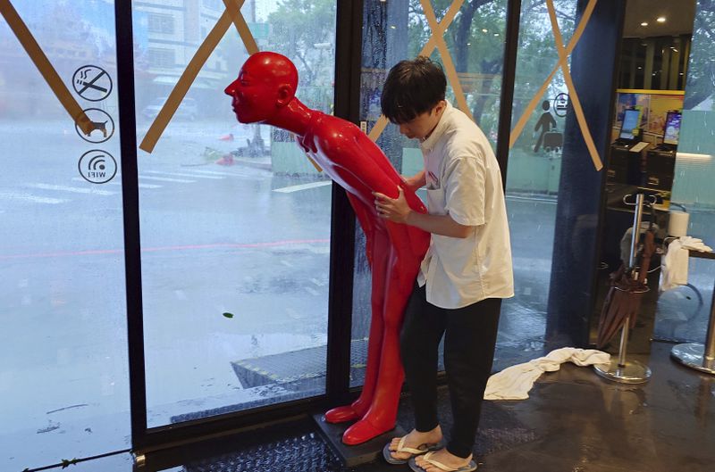 A hotel staff prepares to move a human figure from the doorway to inside as Typhoon Krathon arrives in Kaohsiung, southern Taiwan, Thursday, Oct. 3, 2024. (AP Photo/Chiang Ying-ying)