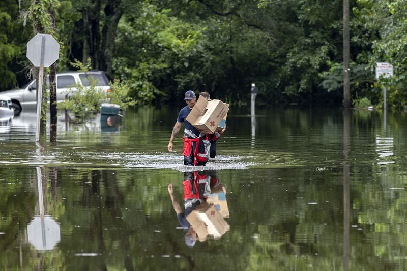 Savannah Fire Advanced Firefighters Andrew Stevenson, front, and Ron Strauss carry food to residents in the Tremont Park neighborhood that where stranded in flooding from Tropical Storm Debby, Tuesday, Aug. 6, 2024, in Savannah, Ga. (AP Photo/Stephen B. Morton)