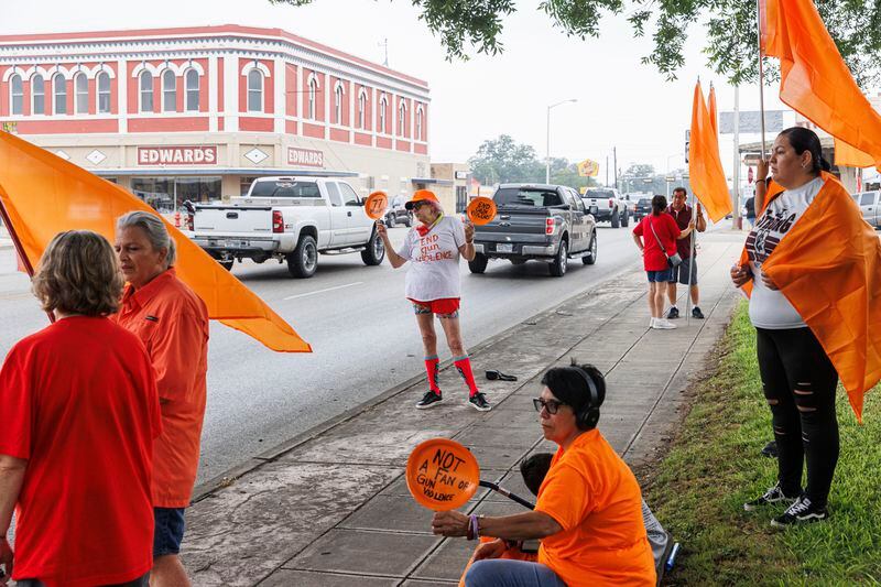 Jan Welch, center, of Austin, and others wave to traffic driving by Main Street during a commemorative gun violence awareness event held at the town square on Friday morning, May 24, 2024, in Uvalde, Texas. Friday marked two years since 19 fourth-graders and two teachers were killed in a mass shooting at Robb Elementary School. (Sam Owens/The San Antonio Express-News via AP)