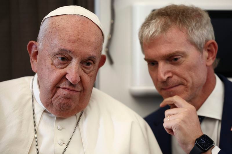 Pope Francis listens to Vatican spokesman Matteo Bruni aboard the papal plane on his flight back after his 12-day journey across Southeast Asia and Oceania, Friday, Sept. 13, 2024. (Guglielmo Mangiapane/Pool Photo via AP)