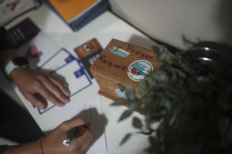 A Surf Church member writes next to a prayer petition box at the church in the suburbs of Porto, Portugal on Sunday, Aug. 18, 2024. (AP Photo/Luis Andres Henao)