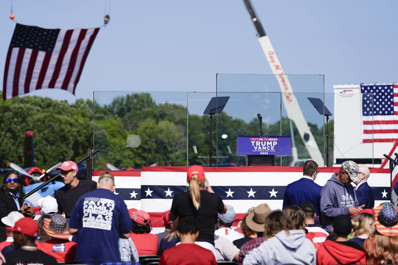 An outdoor stage is set encased with bulletproof glass as supporters arrive to hear Republican presidential nominee former President Donald Trump speak at a rally, Wednesday, Aug. 21, 2024, in Asheboro, N.C. Wednesday's event is the first outdoor rally Trump has held since the attempted assassination of the former president. (AP Photo/Julia Nikhinson)