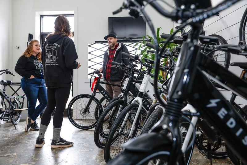 Emily Beach (left) and her husband Jeff (right) chat with Edison Electric Bike Co. shop manager Tyler Riberdy (center) on Thursday, December 22, 2022. (Natrice Miller/natrice.miller@ajc.com)