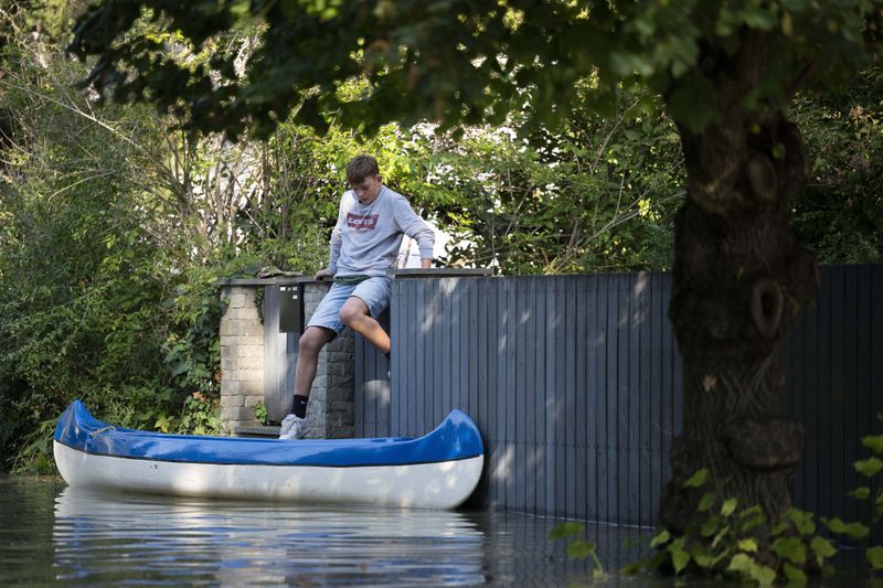 A kid jumps to his canoe from the fence of his flooded house on the outskirts of Szentendre, near Budapest, Hungary, as the Danube river floods its banks on Thursday, Sept. 19, 2024. (AP Photo/Denes Erdos)