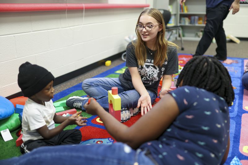 Eighth grade student Grace Polzin plays with 3-year-old Zion Blackman next to his mother Sheldon Blackman at the Play 2 Learn program at Duluth Middle School, Wednesday, Nov. 8, 2023, in Duluth. These students are part of the teaching profession program and have an interest in a career in education. (Jason Getz / Jason.Getz@ajc.com)