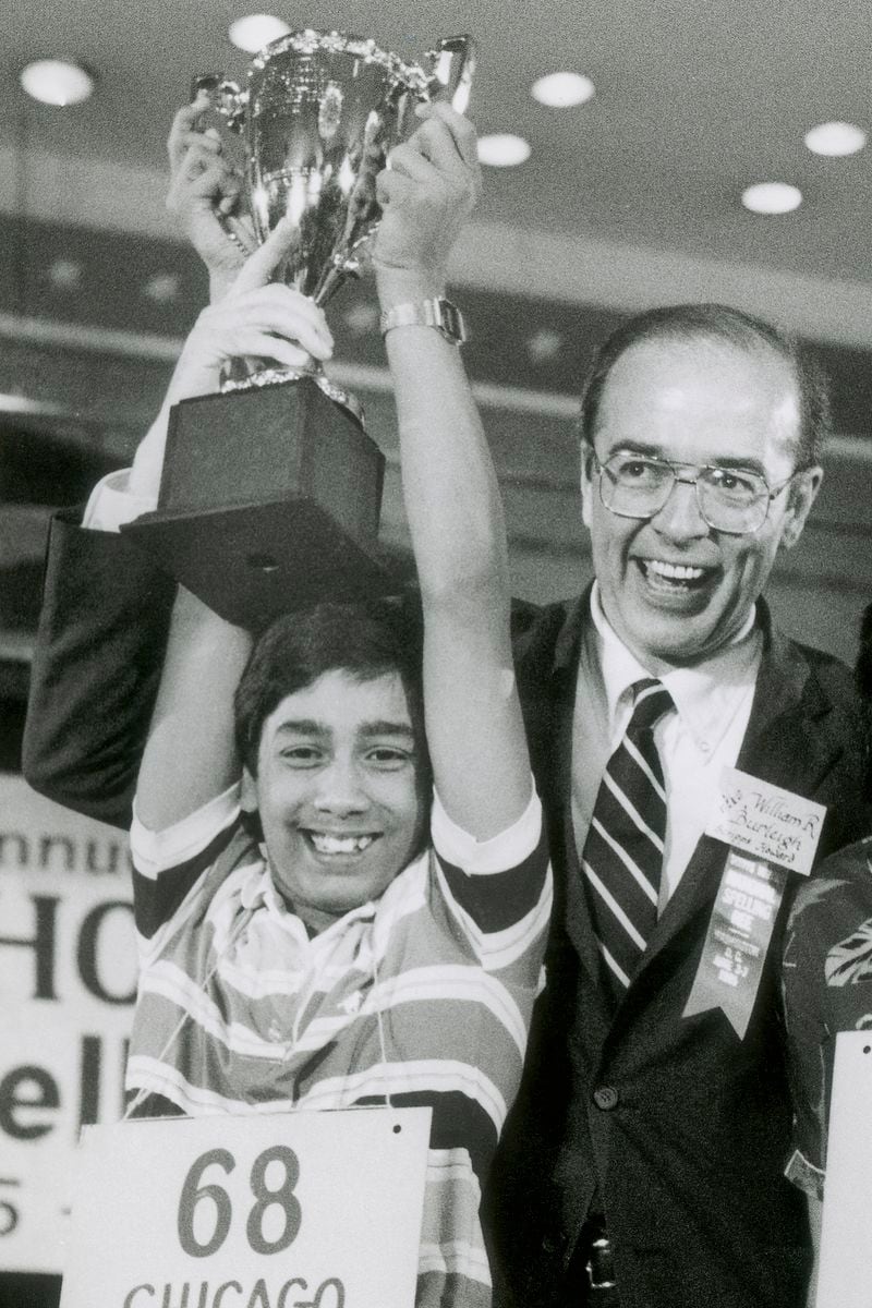 FILE - Balu Natarajan, an 8th grade student at Jefferson Junior High School in Woodbridge, Ill., holds his trophy with the aid of William R. Burleigh, vice president of Scripps Howard Newspapers, sponsor of the National Spelling Bee, after he won the competition in Washington, on June 6, 1985. Since 1999, 28 of the last 34 Scripps National Spelling bee champions have been Indian American. And most of those winners are the offspring of parents who arrived in the United States on student or work visas. The experiences of first-generation Indian Americans and their spelling bee champion children illustrate the economic success and cultural impact of the nation’s second-largest immigrant group. (AP Photo/Bob Daugherty, File)