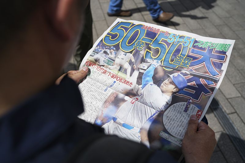 A pedestrian reads an extra edition of the Sports Hochi newspaper reporting on the Los Angeles Dodgers' Shohei Ohtani becoming the first player in major league history with 50 home runs and 50 stolen bases in a season, Friday, Sept. 20, 2024, in Tokyo. (AP Photo/Eugene Hoshiko)