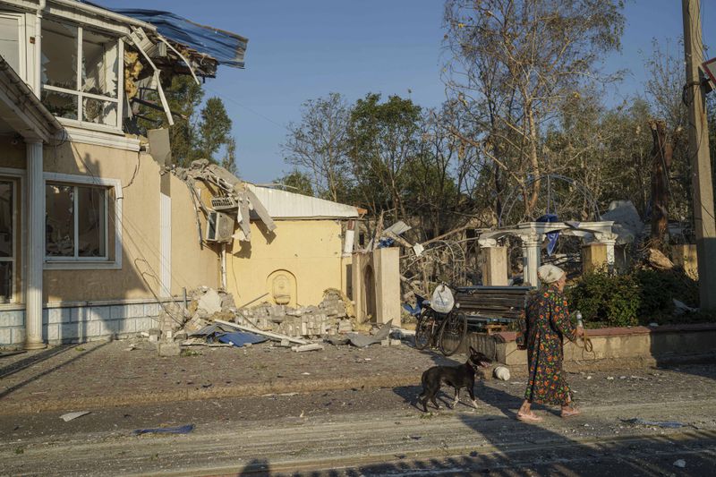 A woman walks with her dog in front of the Sapphire hotel which was destroyed by a Russian rocket attack in Kramatorsk, Donetsk region, Ukraine, Sunday, Aug. 25, 2024. (AP Photo/Evgeniy Maloletka)