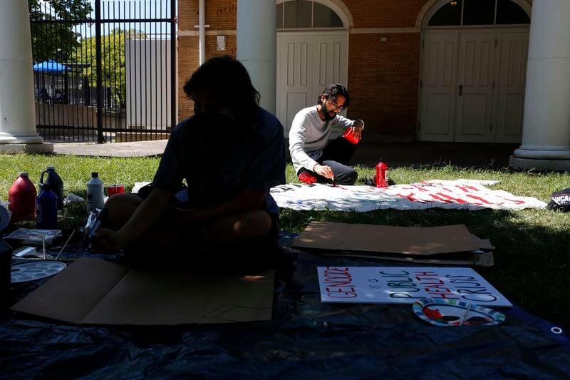 YM Masood, back center, paints a protest sign with another protester on Sunday, Aug. 11, 2024, at a park on Chicago's South Side, ahead of March on DNC protests during the Democratic National Convention. (AP Photo/Martha Irvine)