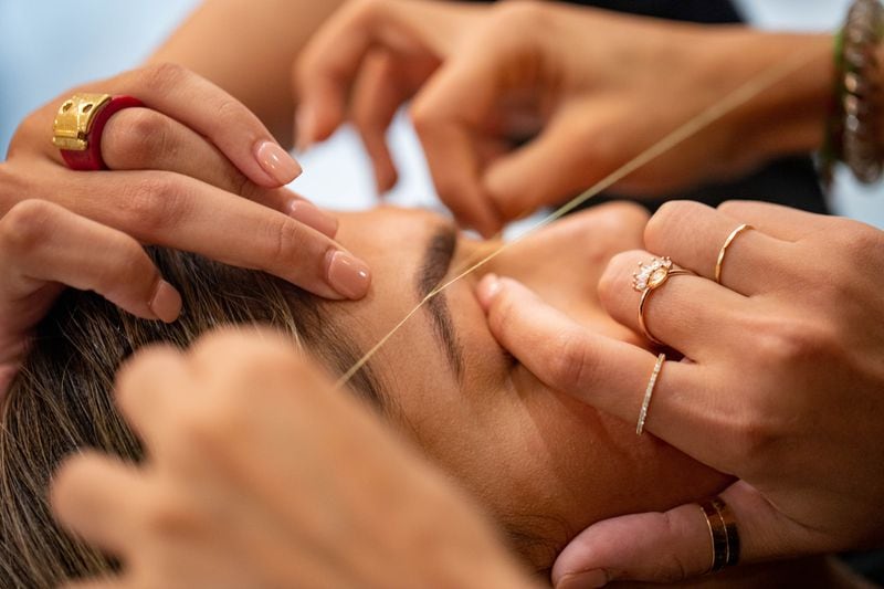 Elnaz Sajadieh has eyebrow threading done by Noureen Wadhavania at Beauty Brow N Beyond on Thursday, Oct 14, 2021.  Sajadieh, who is Iranian American, has been getting her brows threaded by Wadhvania for more than a decade. (Jenni Girtman for The Atlanta Journal-Constitution)