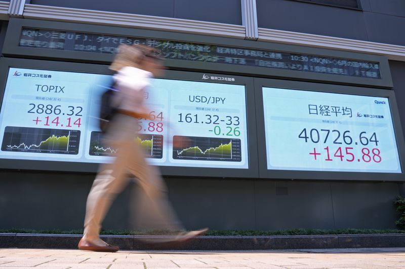 A passerby walks past an electronic stock board showing Japan's Nikkei 225 index, right, at a securities firm Thursday, July 4, 2024 in Tokyo. (AP Photo/Shuji Kajiyama)