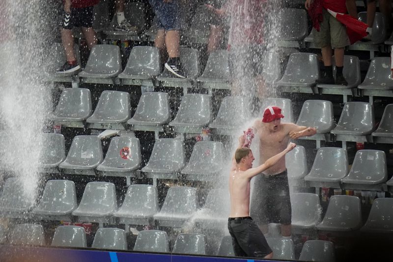 Fans dance in the rain while a round of sixteen match between Germany and Denmark at the Euro 2024 soccer tournament is suspended in Dortmund, Germany, Saturday, June 29, 2024. (AP Photo/Hassan Ammar)