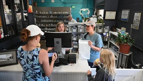 Nikki Bryant (right), independent pharmacist, is shown here this year at Adams Family Pharmacy in Cuthbert, which she owns. She says pharmacy benefit managers pay independent pharmacies so little they are at risk of going out of business. Bryant and Laine Frazier, intern pharmacist, are shown here helping customer Robbin Templey with her granddaughter Ella Ray Buchanan, 10. Bryant now bakes at night in order to supplement her pharmacy's income with sales of cake slices and coffee.  (Photo by Hyosub Shin / AJC)