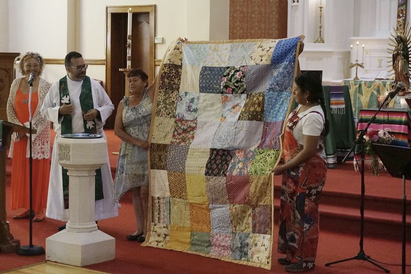 The Rev. Hierald Osorto, second left, Lizete Vega, church council president, right, and others present a quilt blanket made at Iglesia Luterana San Pablo in Minneapolis, on Sept. 8, 2024. The Lutheran congregation, founded by Swedish immigrants in the late 19th-century, is now majority Latino and a statue of the Virgin of Guadalupe stands next to its altar. (AP Photo/Giovanna Dell'Orto)