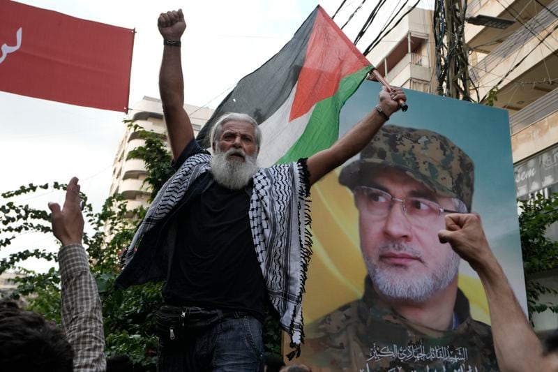 A Hezbollah supporter carries a Palestinian flag near a picture of Hezbollah commander Ibrahim Akil, during Akil's funeral procession in Beirut's southern suburb, Sunday, Sept. 22, 2024. (AP Photo/Bilal Hussein)