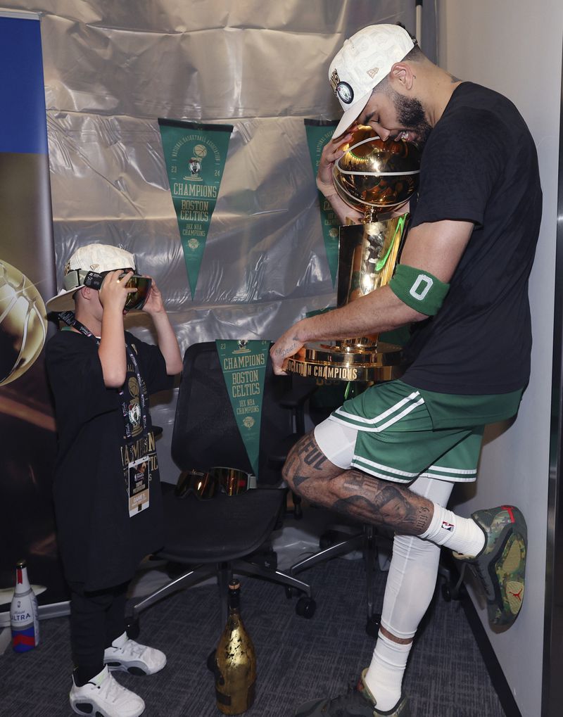 Boston Celtics forward Jayson Tatum embraces the Larry O'Brien Championship Trophy as his son Deuce takes a picture after the Celtics defeated the Dallas Mavericks in Game 5 to win the NBA basketball finals Monday, June 17, 2024, in Boston. (Elsa/Pool Photo via AP)