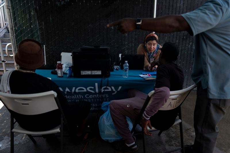 Leida White, an enrollment specialist working for Wesley Health Centers, helps homeless individuals register for medical services outside a mobile clinic in the Skid Row area of Los Angeles, Tuesday, Aug. 27, 2024. (AP Photo/Jae C. Hong)