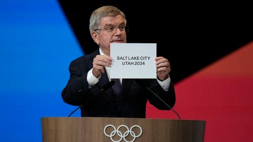 IOC president Thomas Bach holds the board Salt Lake City during the 142nd IOC session at the 2024 Summer Olympics, Wednesday, July 24, 2024, in Paris, France. Salt Lake City was confirmed as host for the 2034 Winter Games by International Olympic Committee. (AP Photo/Natacha Pisarenko, Pool)