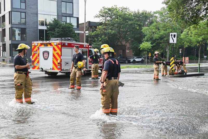 Firefighters survey the scene after a water main break on a street in Montreal, Friday, Aug. 16, 2024, causing flooding in several streets of the area. (Graham Hughes/The Canadian Press via AP)