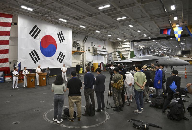 Crew members and member of the media gather in the hanger of the Theodore Roosevelt (CVN 71), a nuclear-powered aircraft carrier, anchored in Busan Naval Base in Busan, South Korea Saturday, June 22, 2024. (Song Kyung-Seok/Pool Photo via AP)
