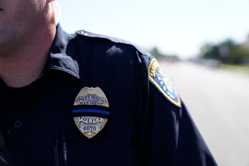 A San Diego police officer wears a band over his badge in honor of a fellow officer killed in an overnight crash at the scene of the accident Tuesday, Aug. 27, 2024, in San Diego. (AP Photo/Gregory Bull)