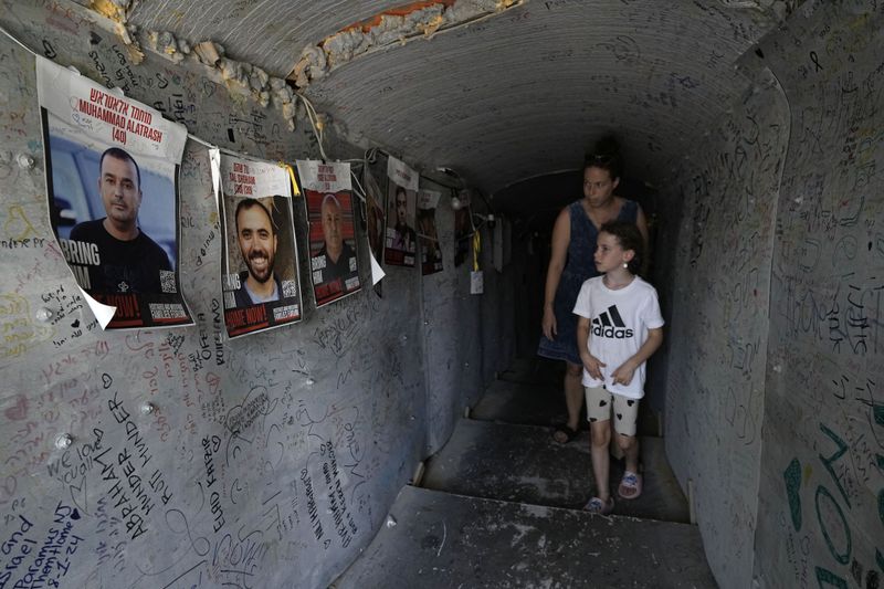 A woman and child walk through a replica of a tunnel used by Hamas militants in the Gaza Strip, ahead of a weekly protest by families of hostages held by the group to demand their release, in Tel Aviv, Israel, Saturday, Aug. 17, 2024. (AP Photo/Tsafrir Abayov)