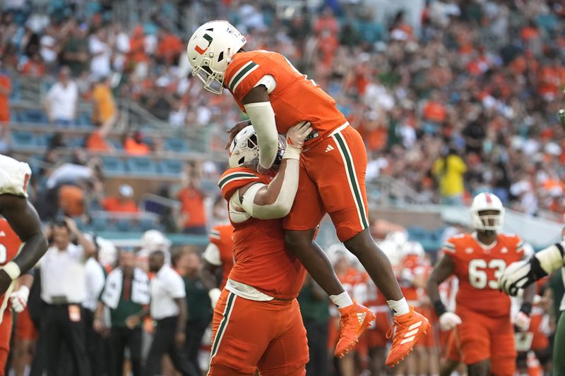 Miami offensive lineman Francis Mauigoa, left, lifts quarterback Cam Ward (1) after Ward threw a touchdown pass to running back Chris Johnson Jr. during the first half of an NCAA football game against Florida A&M, Saturday, Sept. 7, 2024, in Miami Gardens, Fla. (AP Photo/Lynne Sladky)